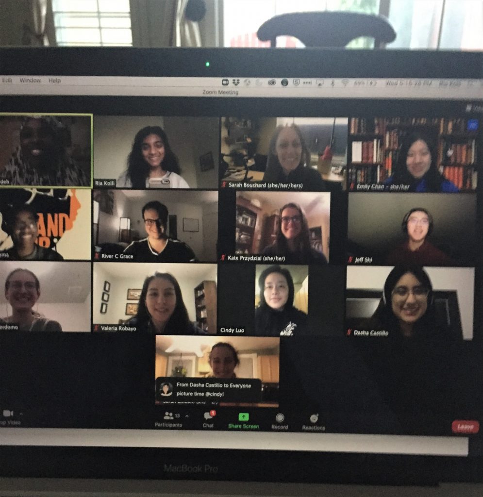 A photo of a laptop screen showing a zoom call with 13 people. A chat message reads "picture time @cindy!" and all the participants are smiling for the photo.