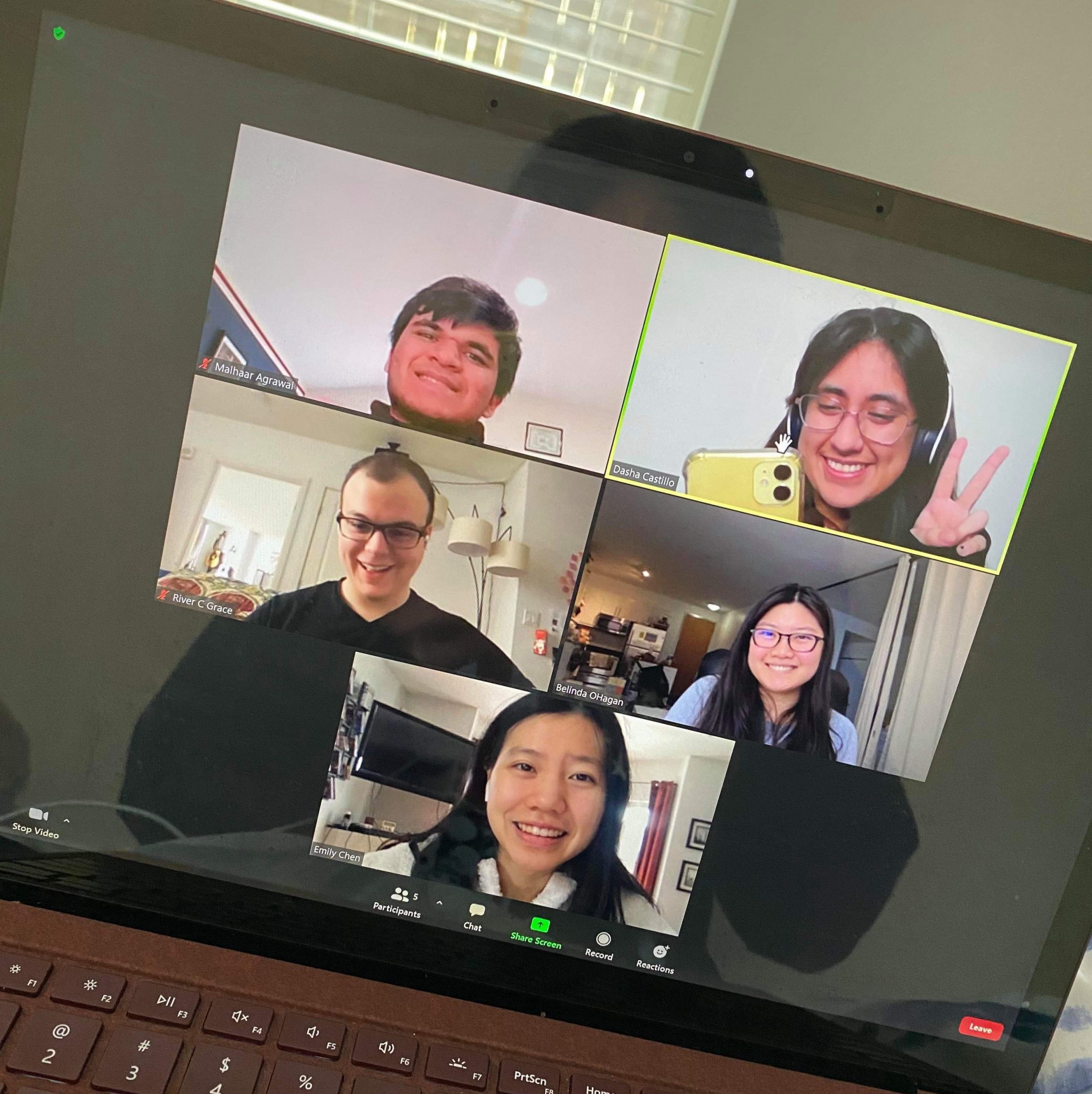 A photo of a laptop screen picturing a zoom call with 5 people, all posing for the photo.